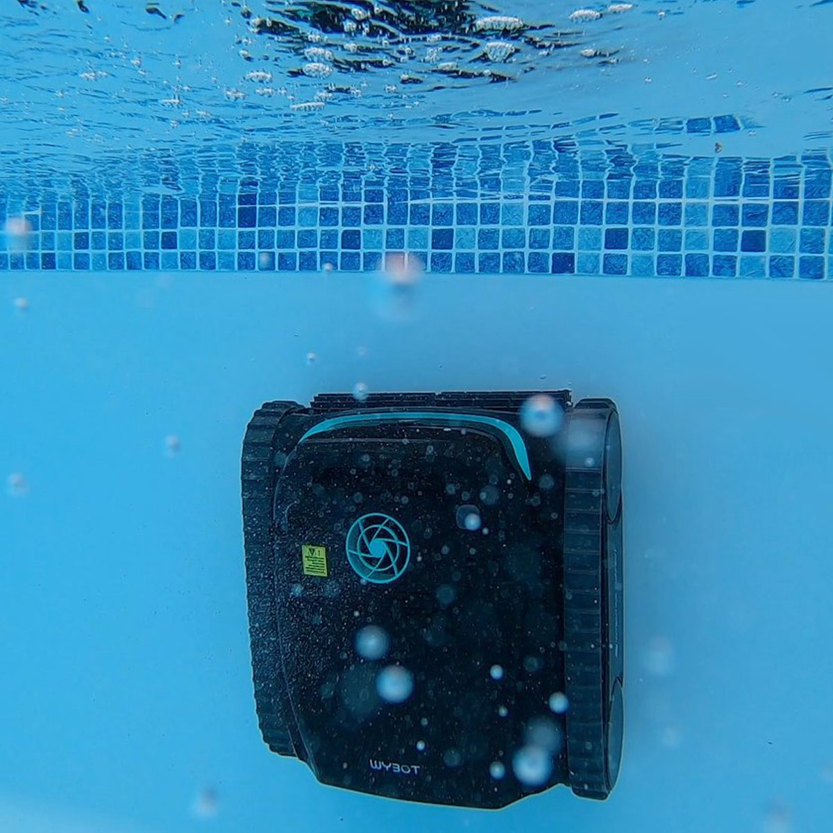 A robotic pool cleaner underwater against a tiled wall